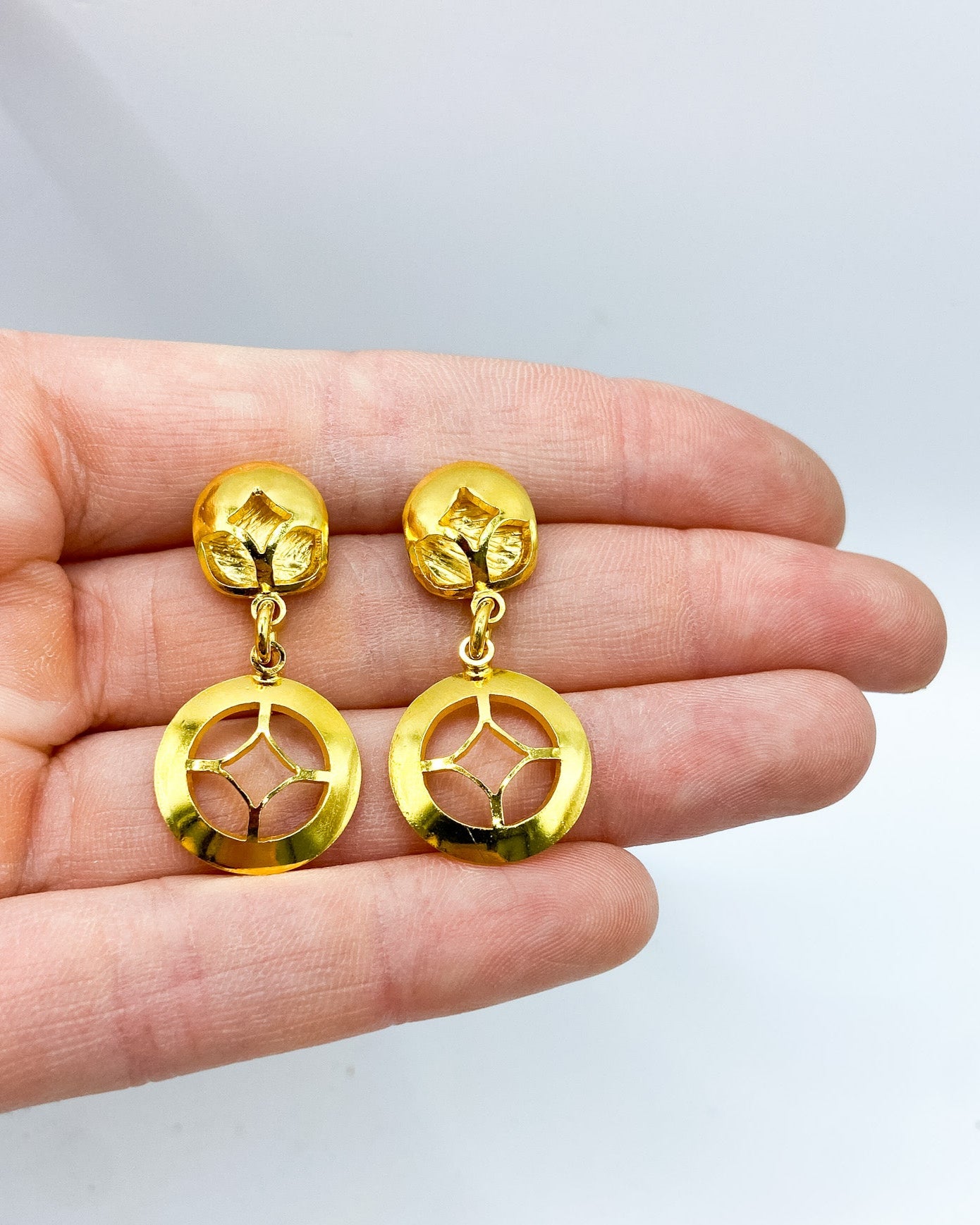 Gold earrings held in a hand against a white background