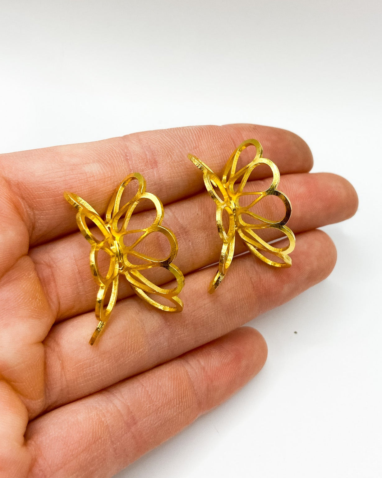 Gold butterfly-shaped earrings held in a hand on a white background