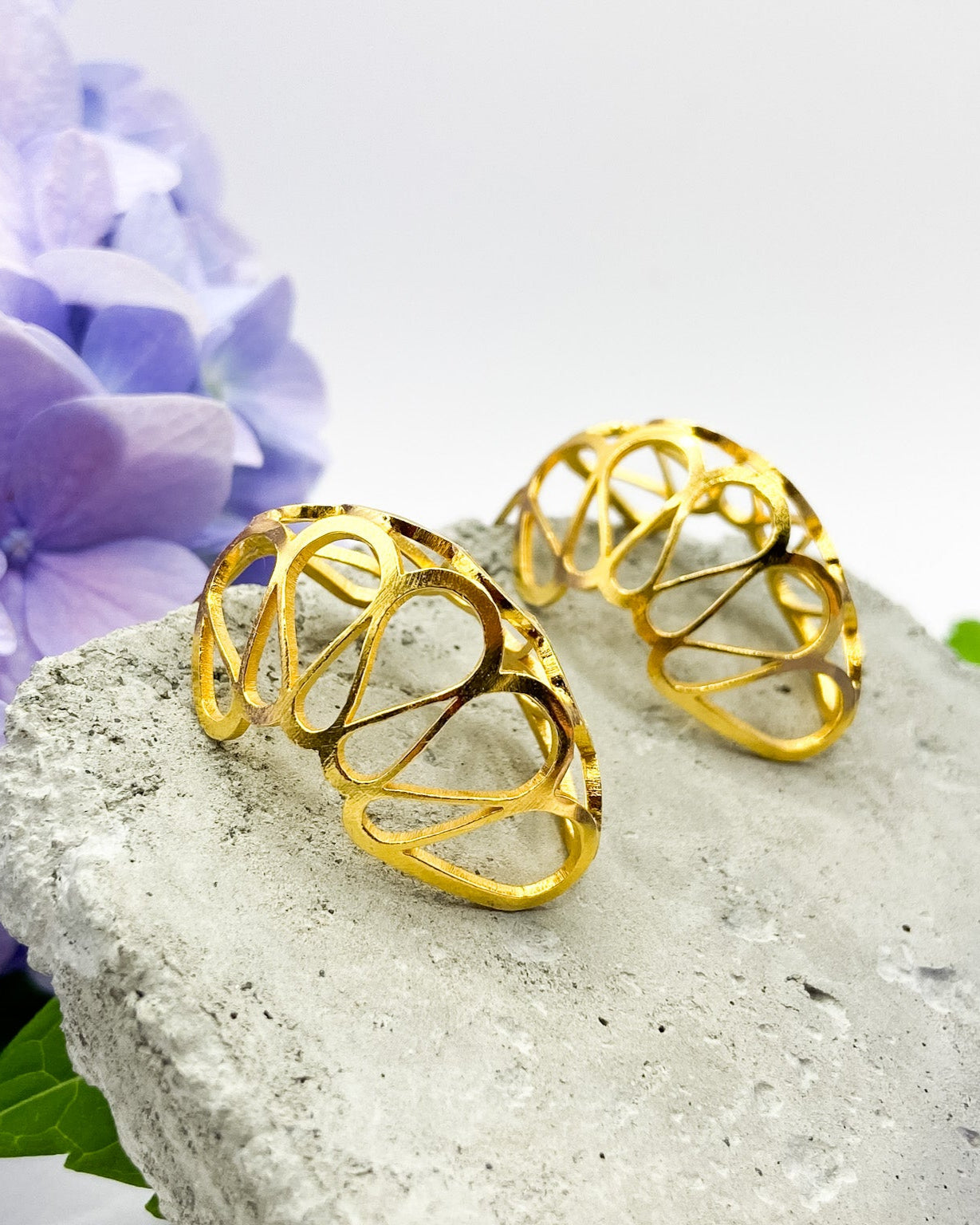 Gold hoop earrings on a stone surface with purple flowers in the background
