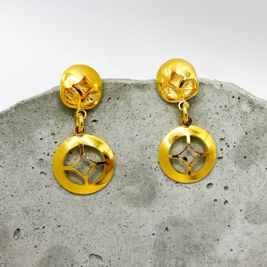 Gold earrings on a textured gray surface with a white background