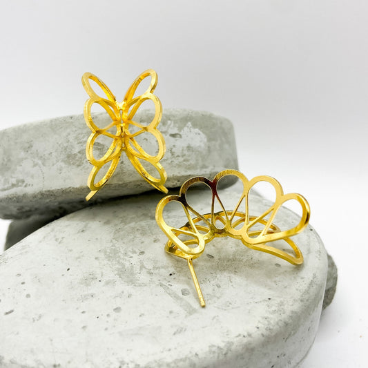 Gold butterfly-shaped earrings on a textured stone surface with a white background