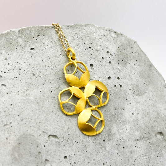 Gold necklace with geometric pendants on a textured stone surface