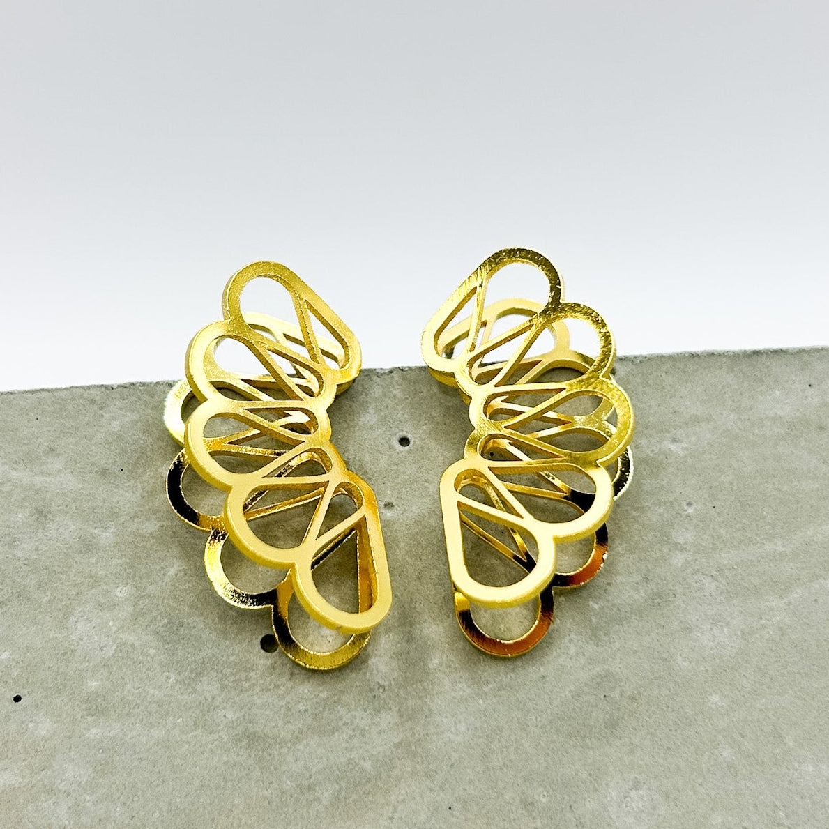 Gold earrings on a textured gray surface with a light gray background