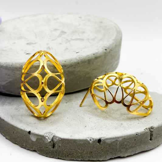 Gold earrings on a concrete surface with a purple flower in the background